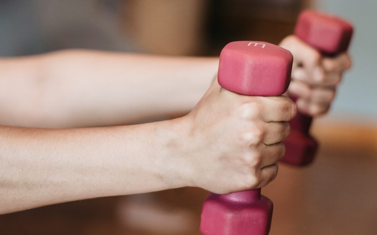 person holding pink and white dumbbells